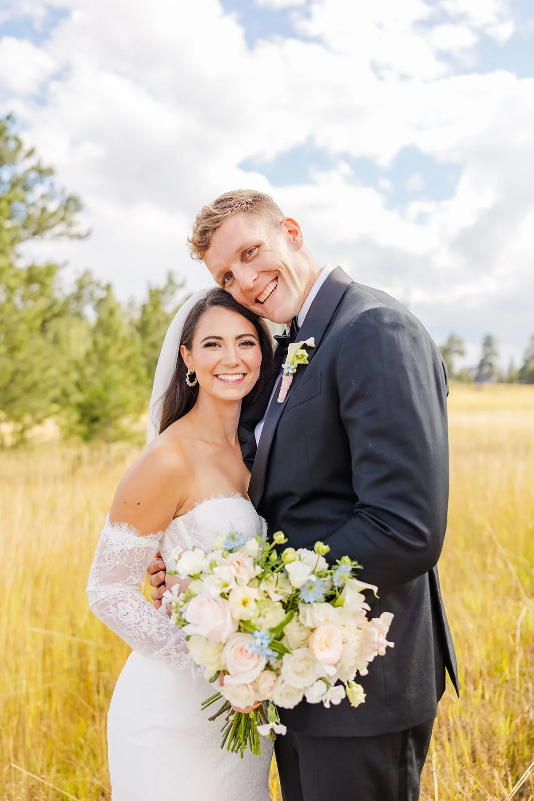 Bride and groom smiling outdoors with white bouquet