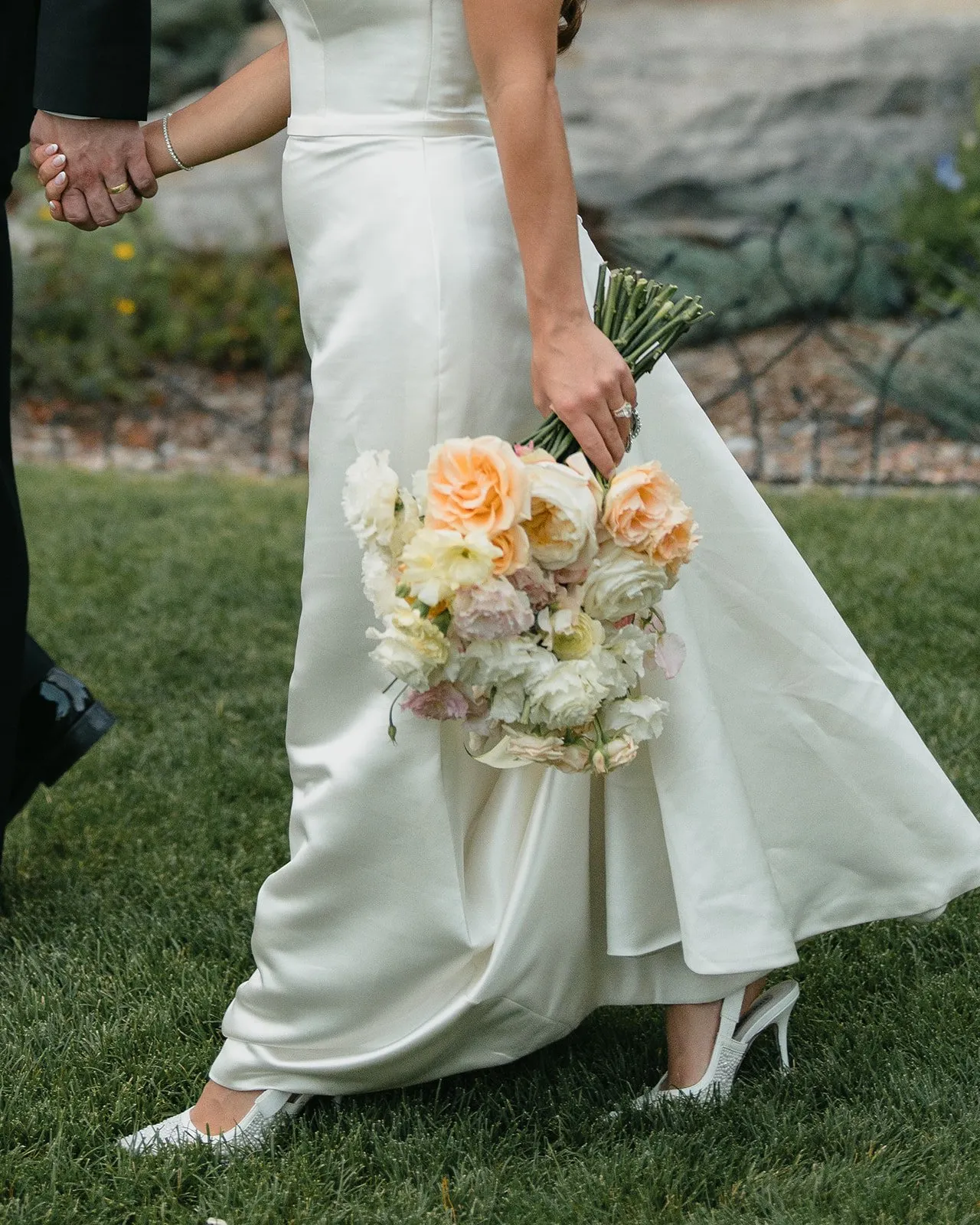 Bride in white dress with peach and white bouquet on outdoor grass