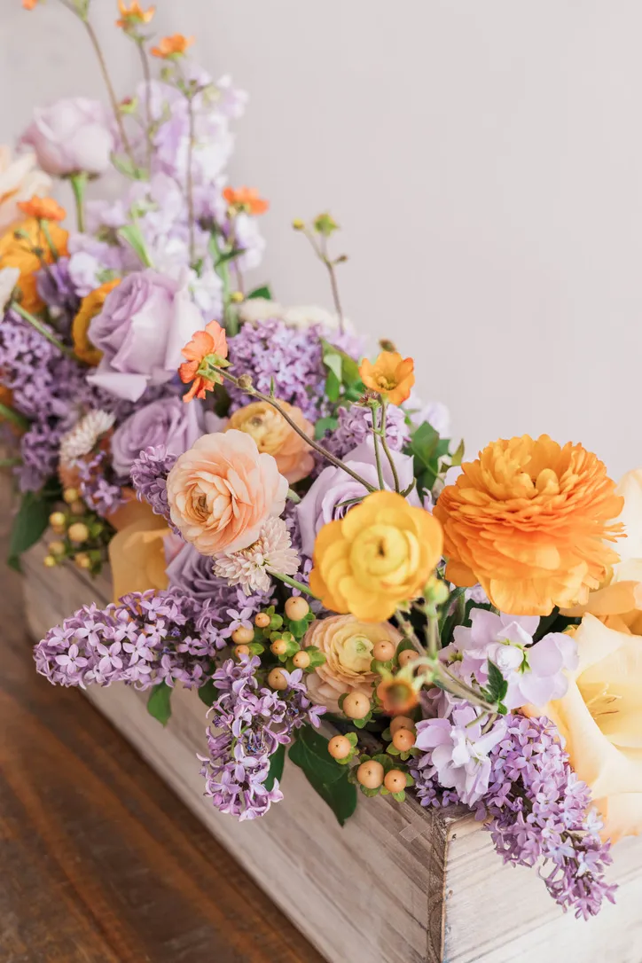 Colorful floral arrangement in wooden box with purple, orange, and yellow