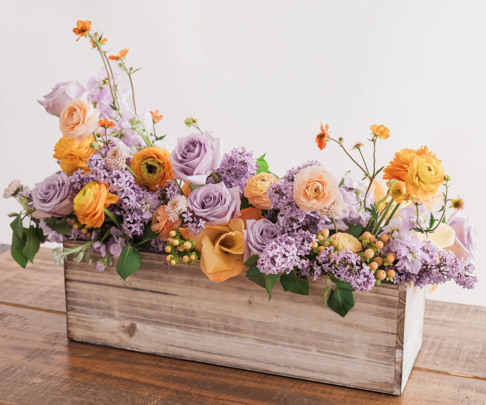 Colorful lilac, orange, and peach floral arrangement in a wooden box