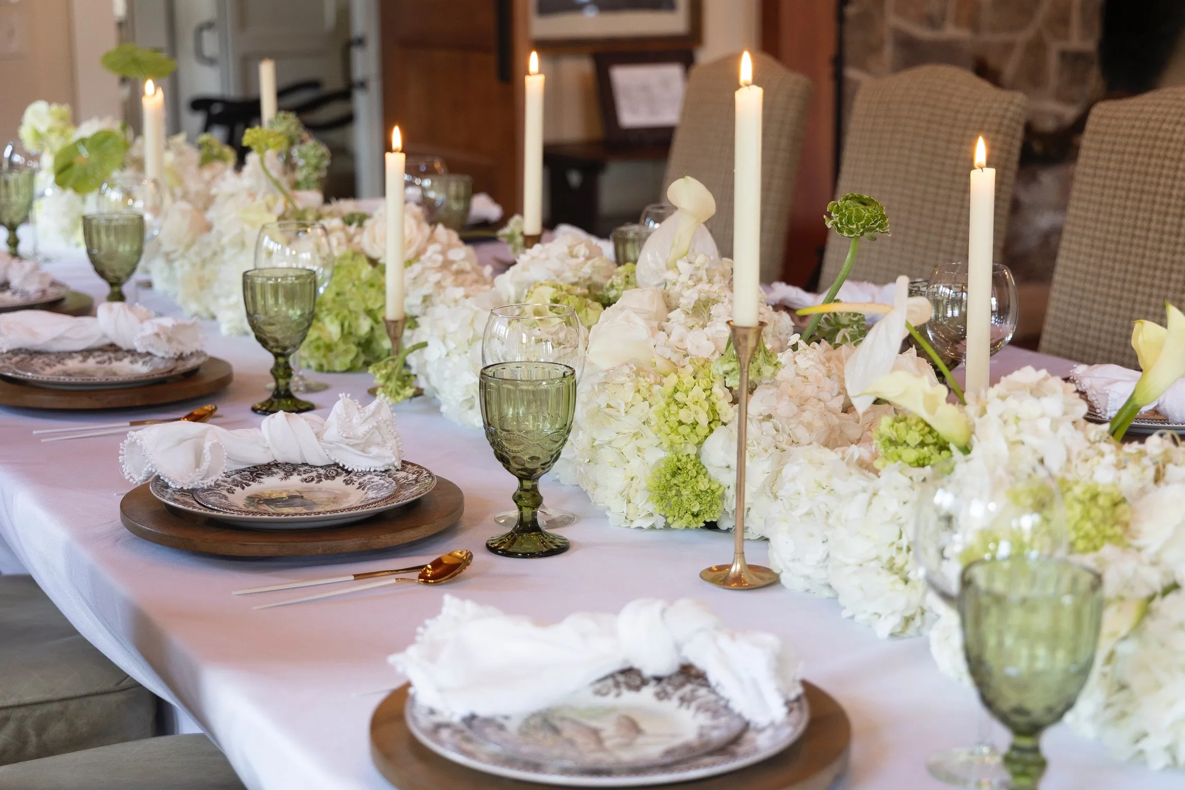 Elegant dinner table with white and green florals, tall candles, and green goblets